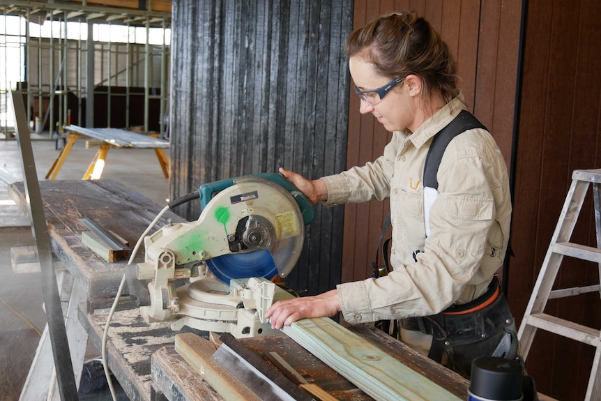 A woman cuts timber with a circular saw inside a construction site