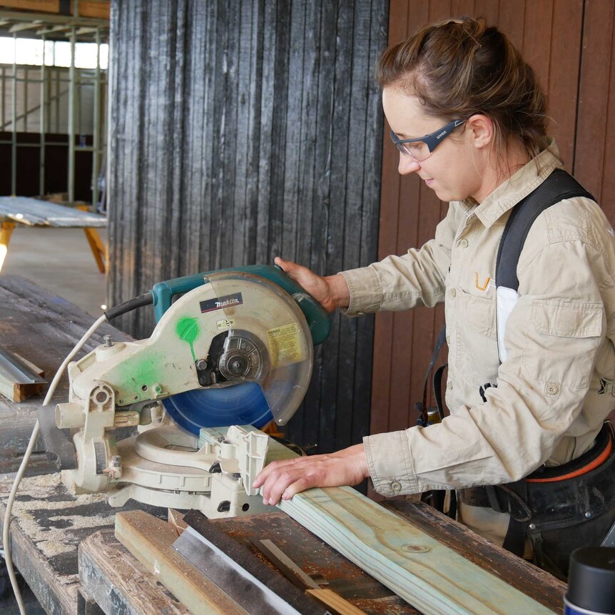 A woman cuts timber with a circular saw inside a construction site