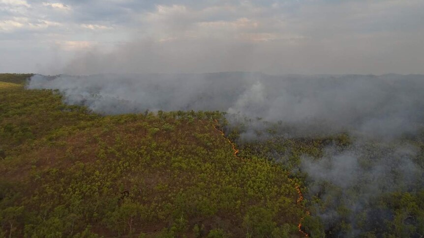 Red snaking line of fire and smoke billow up from tree lined hills in far north Queensland savanna country