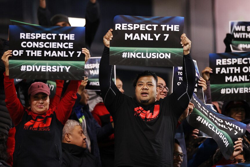 Fans of a sports team hold up signs during a game of NRL