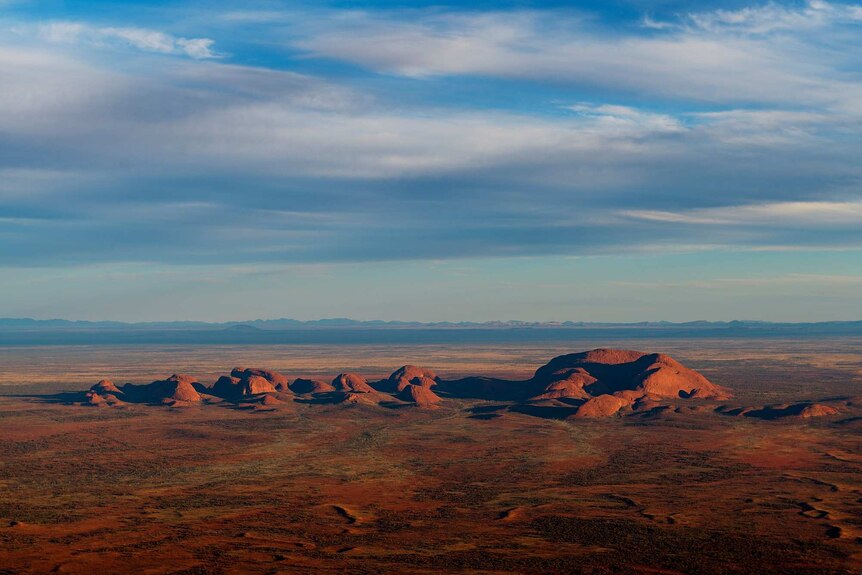 The desert landscape between Docker River and Yulara shows rock formations and mountains on the horizon.