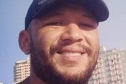 A smiling man wearing a cap and standing outside a large hotel.