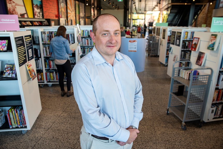 A man stands in front of shelves of books with people browsing in the background.