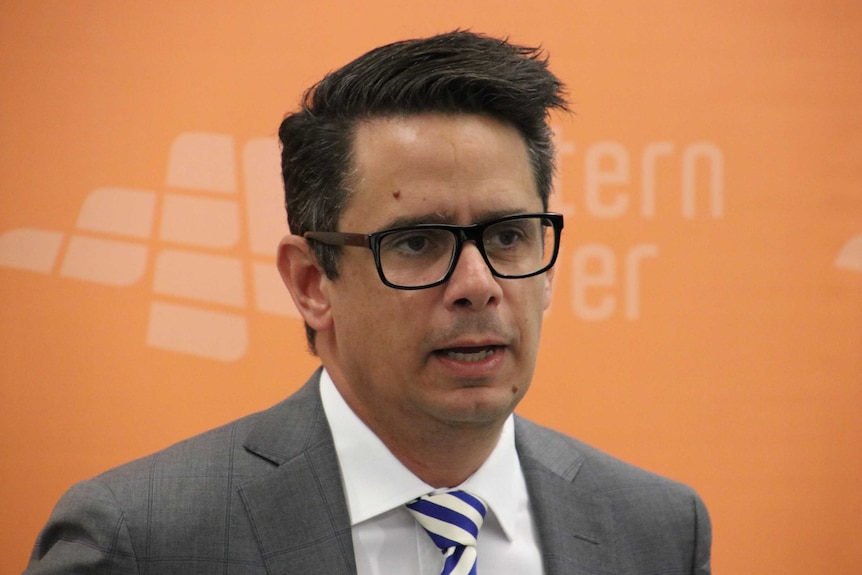 Treasurer Ben Wyatt pictured in front of an orange Western Power banner at a press conference