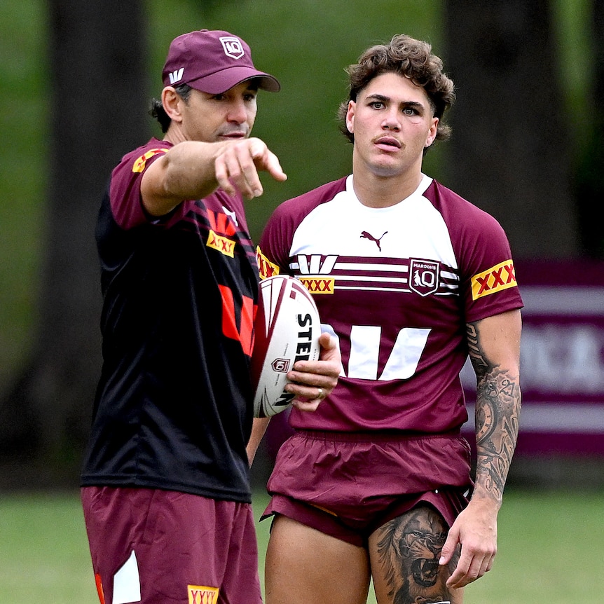 Queensland Maroons coach Billy Slater points while holding a ball in front of fullback Reece Walsh at State of Origin training.