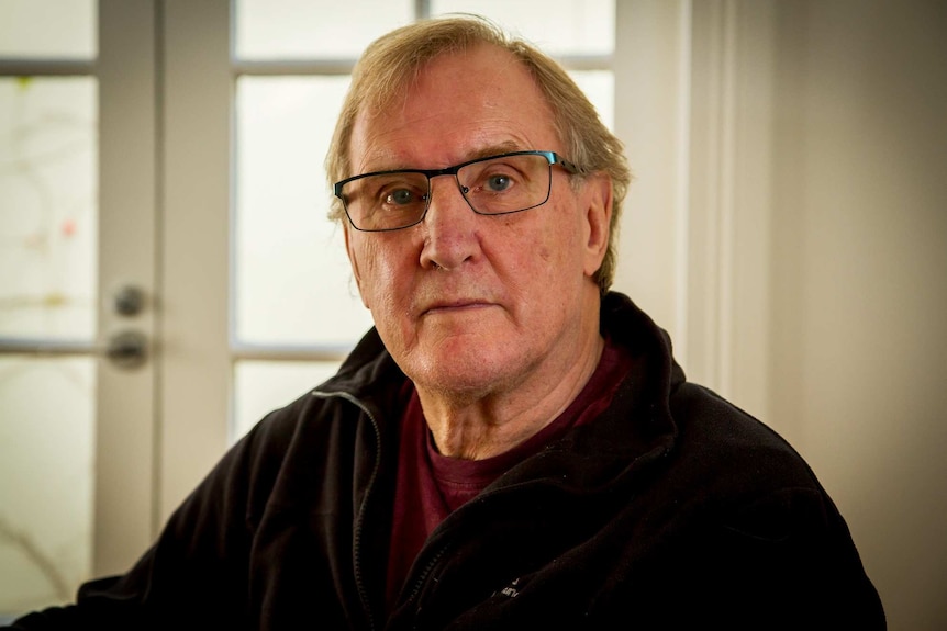 Graeme, dressed in a black jumper and glasses, looks at the camera.