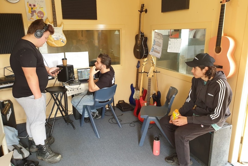 One young man with headphones reads from a phone, while musician Tasman Keith listens to him