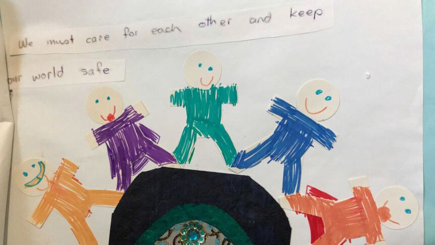 A child's drawing of five people standing on a mound says: "We must care for each other and keep our world safe"