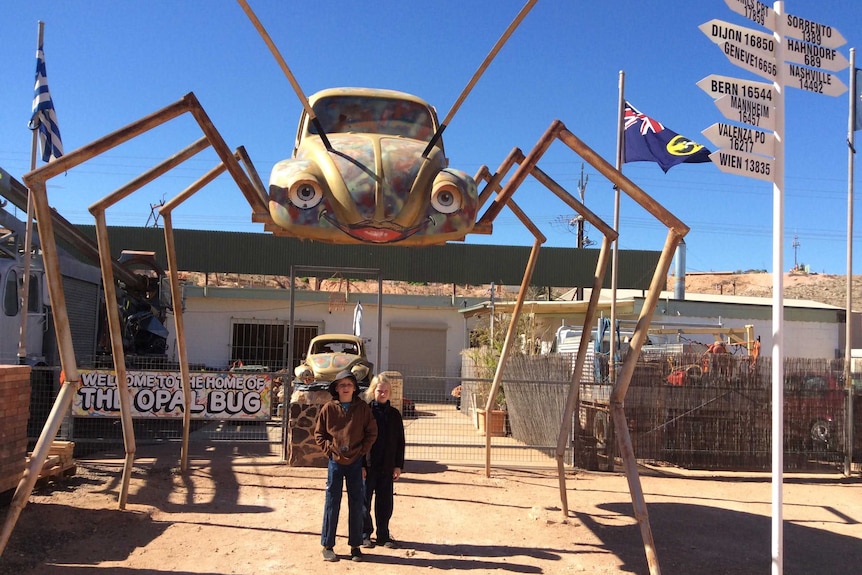 Two boys under sculpture of VB beetle suspended on legs, like giant spider