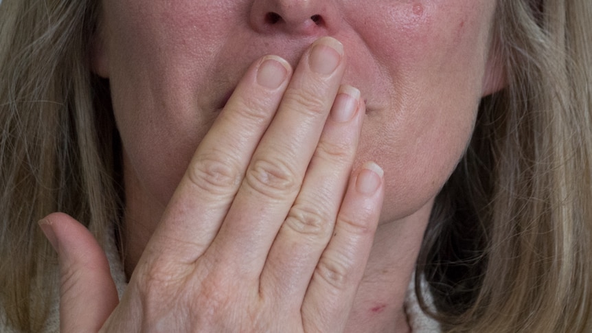 Young woman with hiccups covers her mouth.