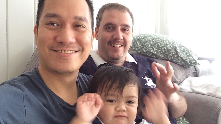 Two men smiling while holding their son.