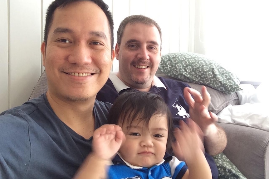 Two men smiling while holding their son.