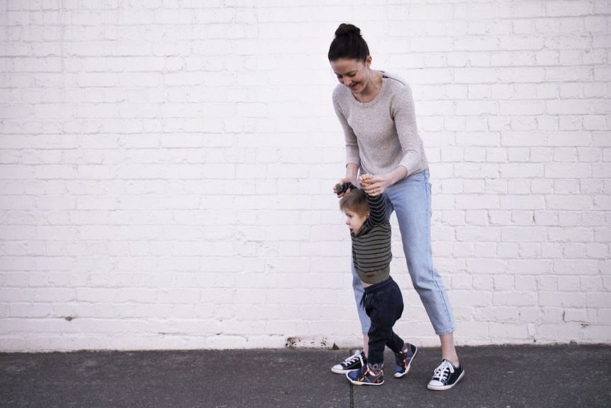 Woman holds the hands of a child as he practices walking.