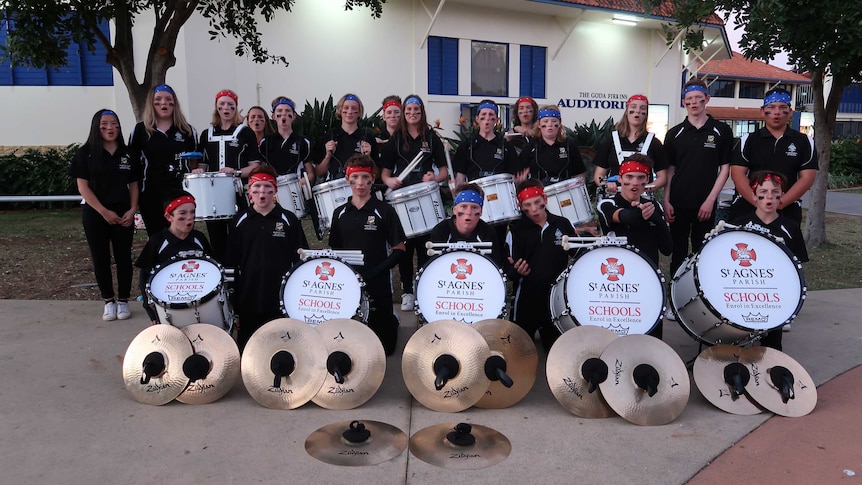 Group of students wearing black shirts and black or red bandanas stand in a group with their drums.