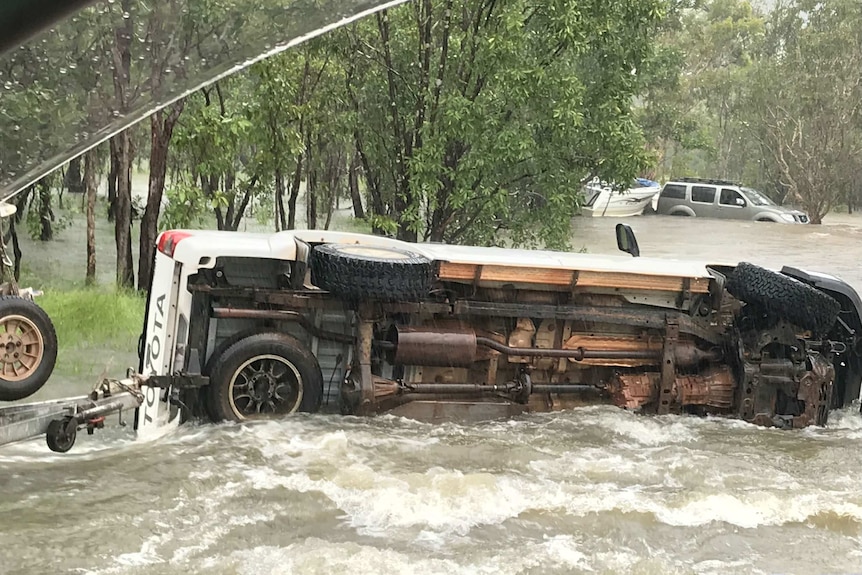 A 4wd ute overturned in floodwaters with another vehicle in the background in water.