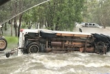 A 4wd ute overturned in floodwaters with another vehicle in the background in water.