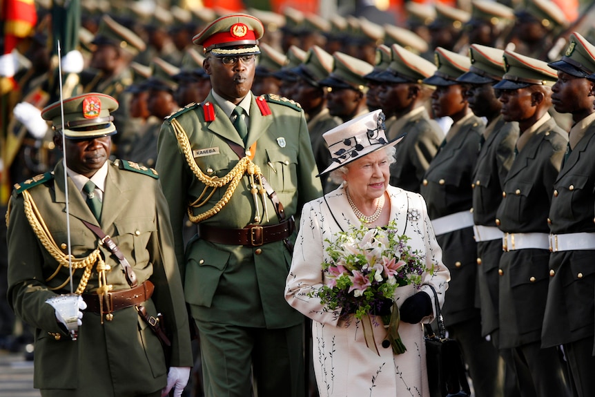 queen in pink holding flowers with ugandan military behind her and forming guard of honour