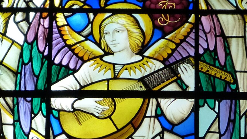 A close-up section of a stained glass window with an Angel playing a lute.
