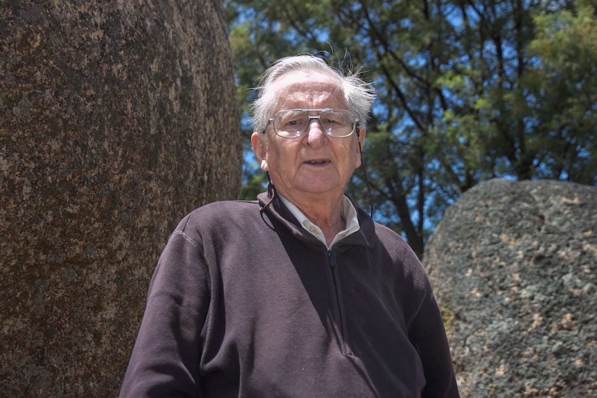 An older man standing in front of two large boulders