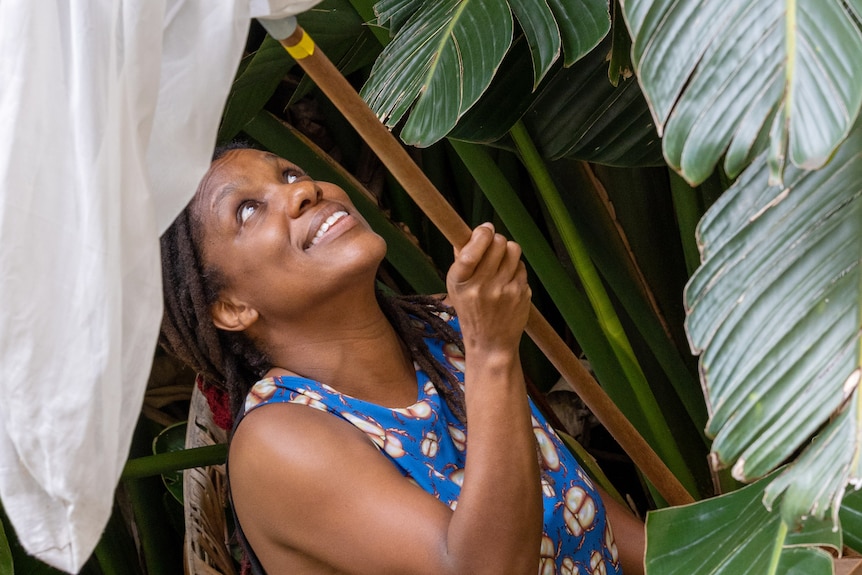 A young woman looks up at large palm leaves with a bug net held aloft