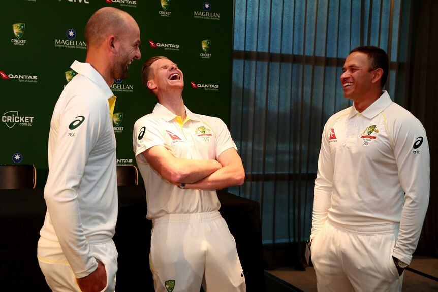 Three men in white cricket uniforms share a joke
