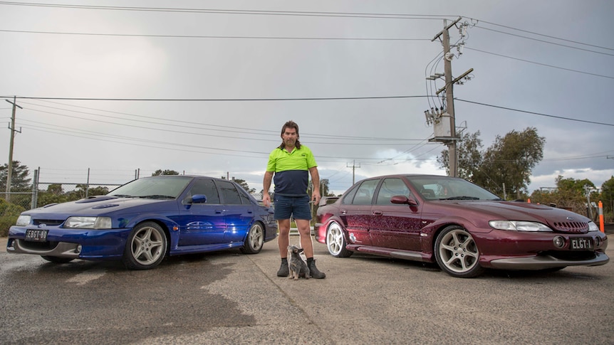 A man stands between his two Ford sedans: a blue 1992 EB and a red 1997 EL GT.