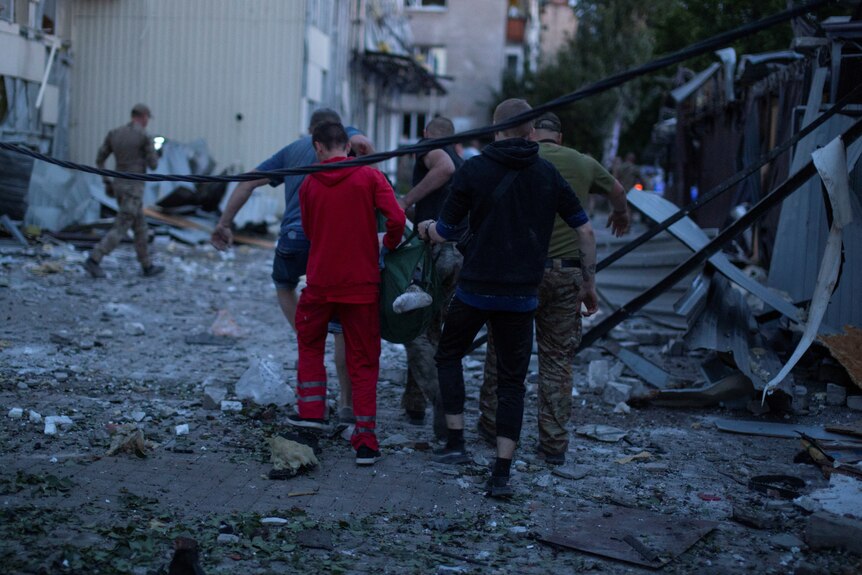 People carry a person on a makeshift stretcher amid rubble and dangling wires.