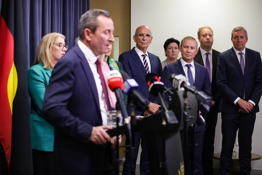 WA Premier Mark McGowan speaks a media conference indoors with his Labor cabinet colleagues watching on from the side.