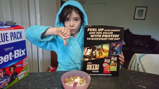 Daliah Lee wears a blue dressing gown as she gestures thumbs down while holding a box of nutrigrain with all men on the back