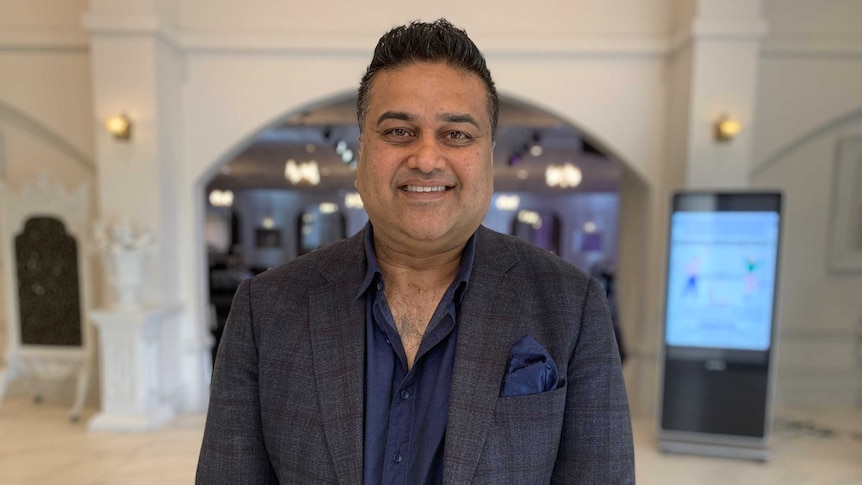 Jude De Silva standing in the entrance to a venue, with a warm happy smile and wearing a dark jacket and navy button-up shirt.