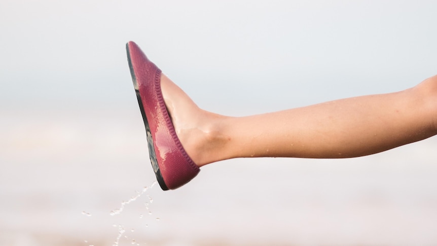 A woman's leg in a red show with a flat heal kicks in the air over a puddle