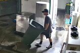 A man pushes a wheelie bin through a butcher shop.