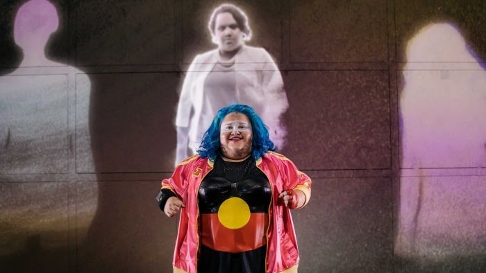 A woman wearing clothes printed with the Indigenous flag performs on stage.