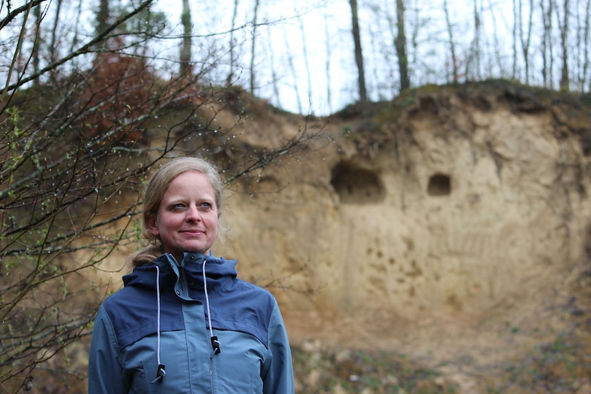 Dr Eck surrounded by trees with a wall of the sand pit behind her