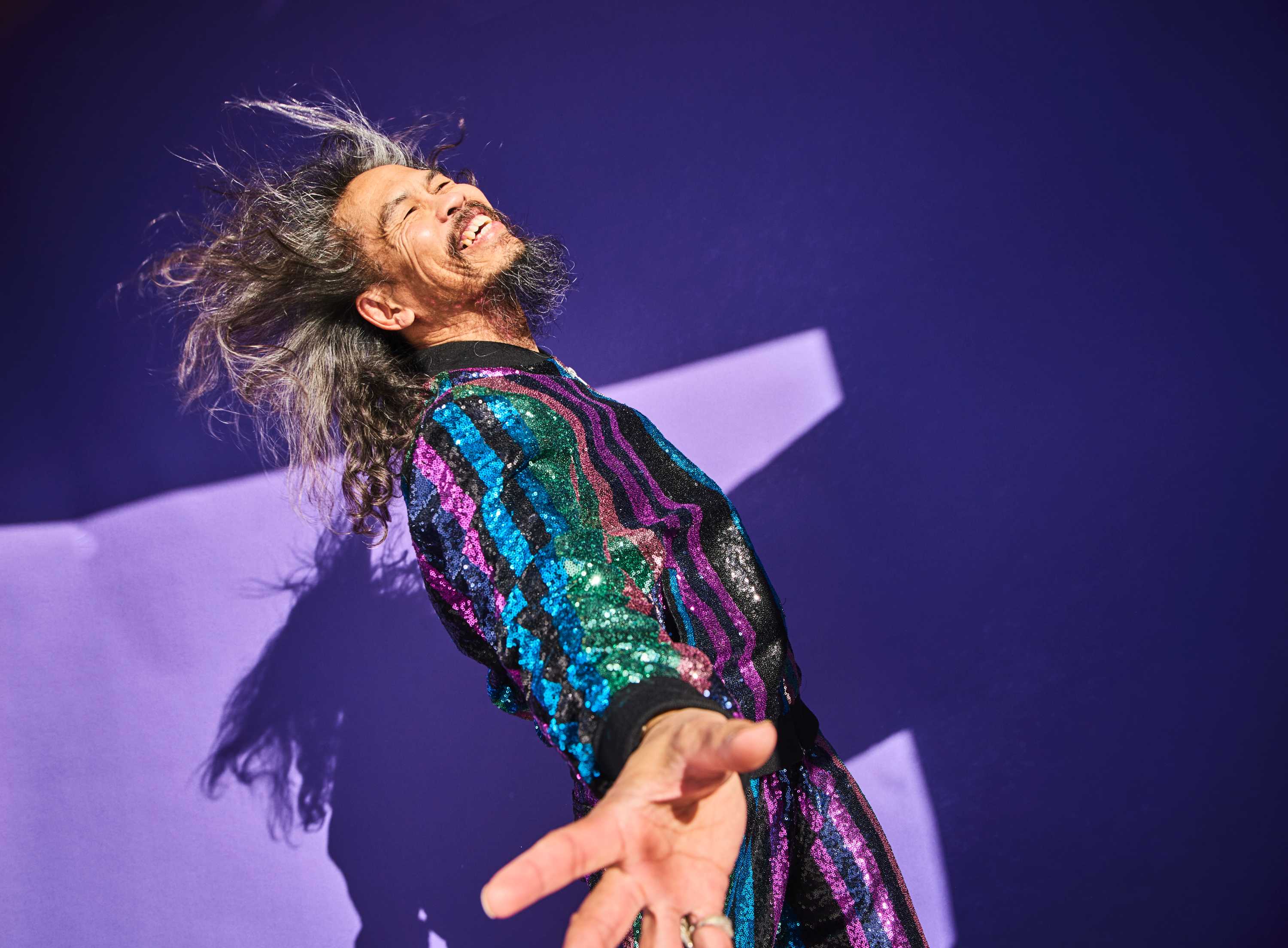 Older man wearing a multicoloured sequin jacket and smiling