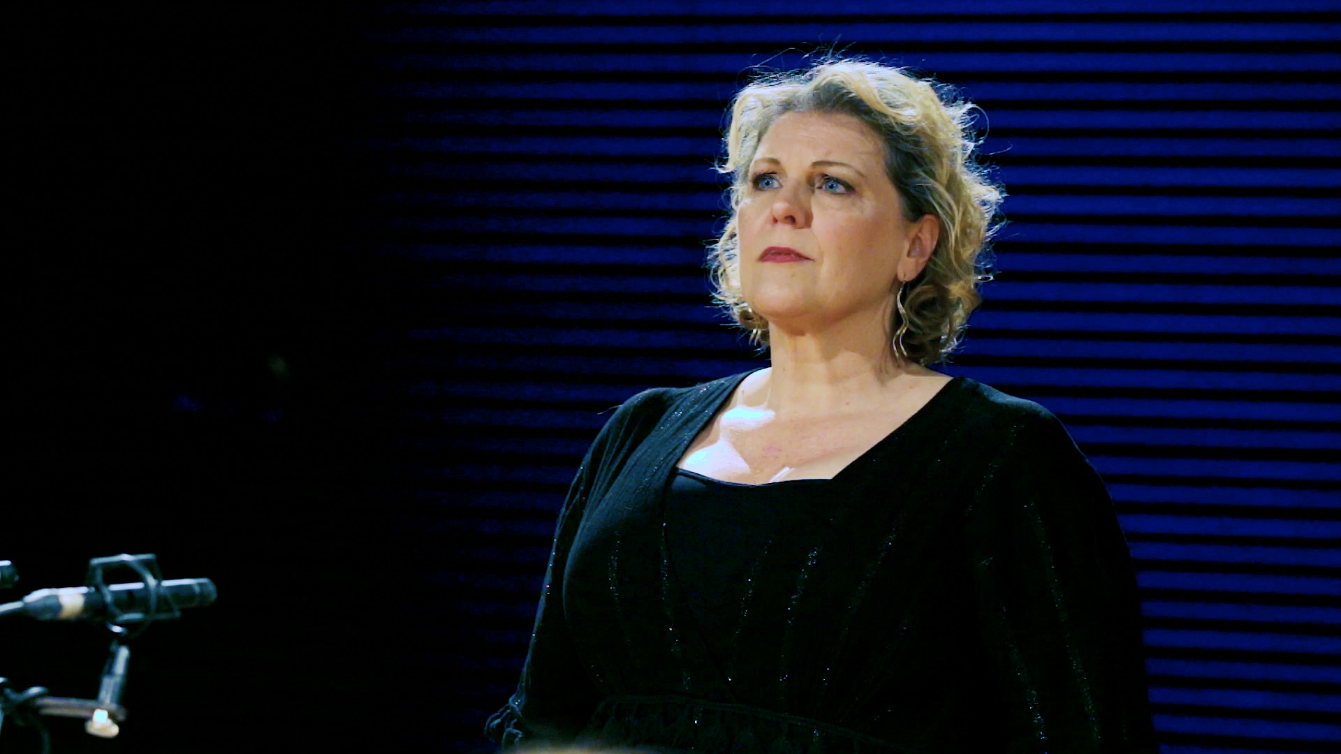 A singer performing in a recording studio by some microphones.