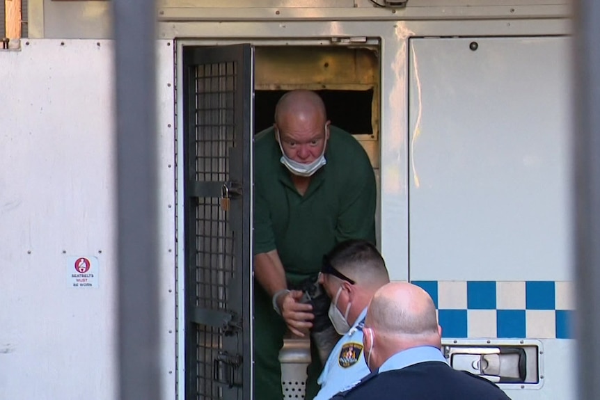 a man with hands in cuffs walking out of a police van