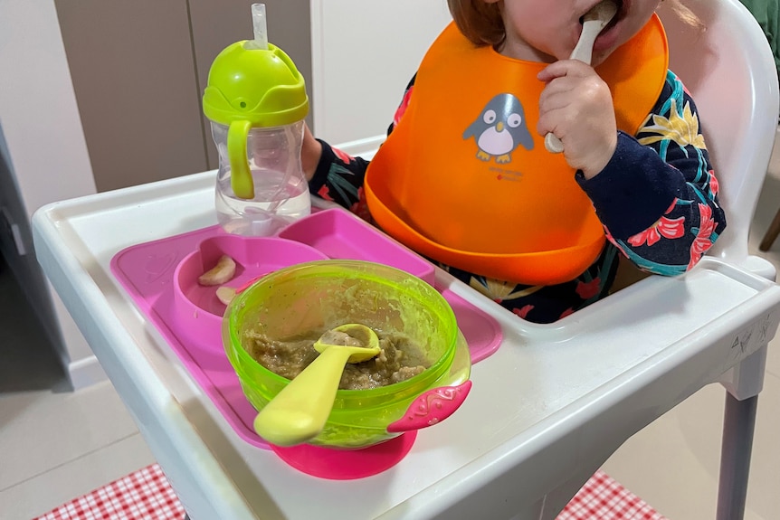Toddler eating with a spoon out of a bowl.