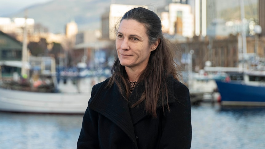 A woman looks off camera standing in front of the Hobart waterfront