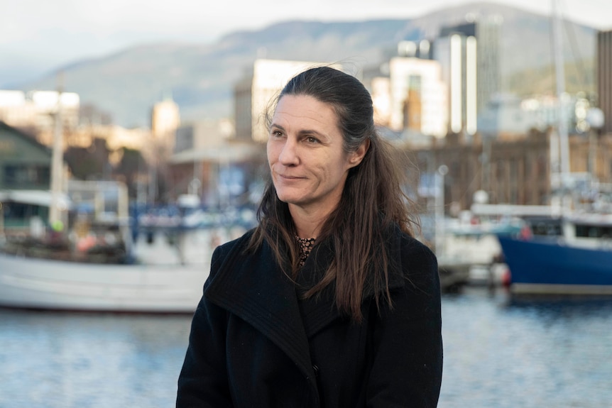 A woman looks off camera standing in front of the Hobart waterfront