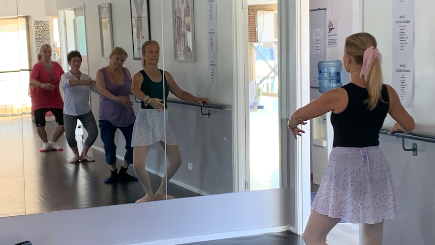 Mirror reflection of four senior ladies using bar to practice ballet poses