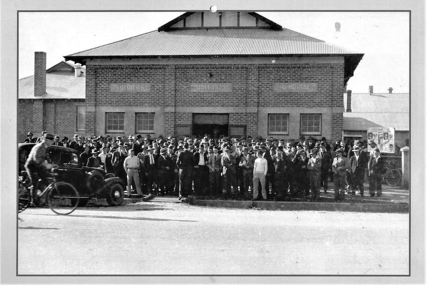 Black and white photo, circa 1938, with a large number of people gathered in front of a memorial hall 