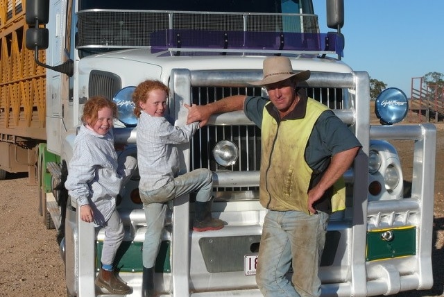 Two young red-headed girls climb on a cattle truck beside their dad.