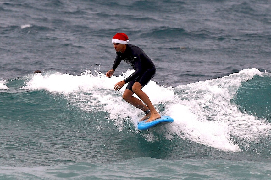 A surfer wearing a Christmas hat rides a wave on his surfboard on Christmas Day at Sydney's Bondi Beach
