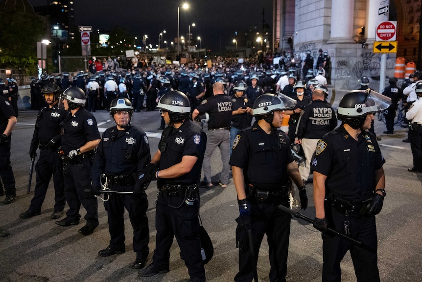 A large group of police wearing helmets and carrying clubs form up as they prepare to engage demonstrators.