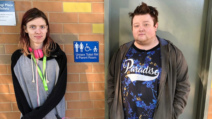 two transgender people from mildura standing in front of a unisex toilet