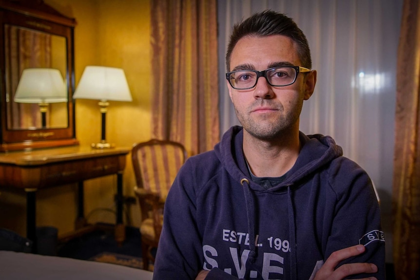 A man in glasses stares directly at the camera with his arms crossed.