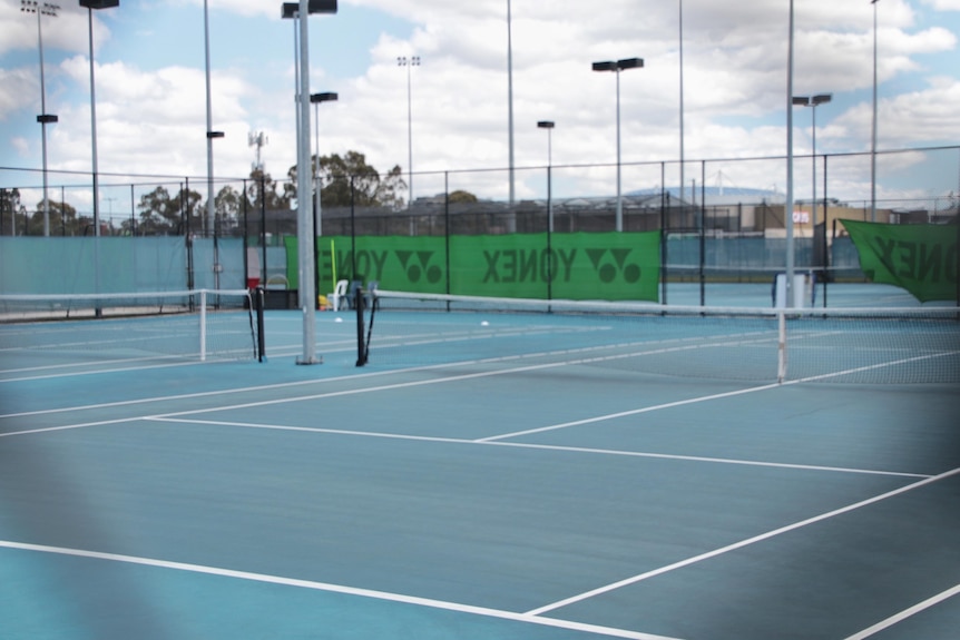 A blue sports court with nets and lighting at a high school.