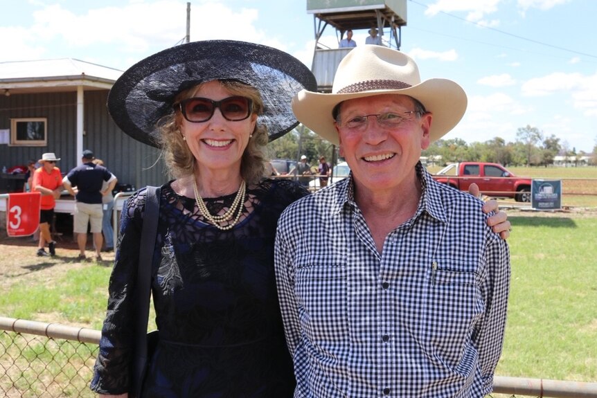 An older man and woman, both wearing hats, at a country race meet