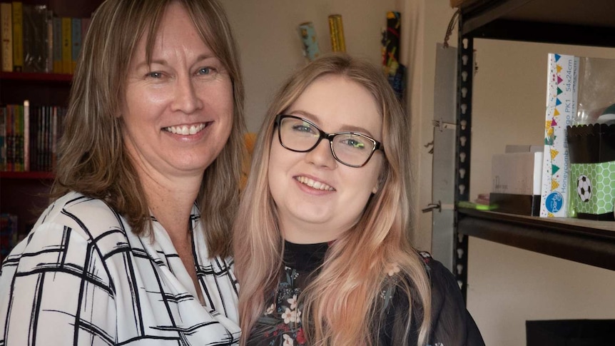 Two women smiling side by side next to shelf of presents and party supplies